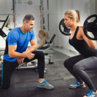 Woman does squat with trainer at gym